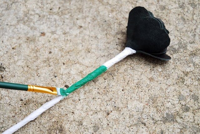 a paintbrush adds green paint to tissue paper wrapped around the stem of a homemade craft flower.