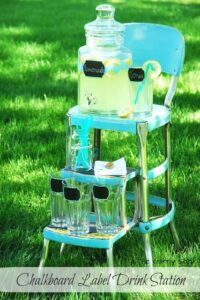 Lemonade in drink dispensers and glasses set on an old metal step stool.