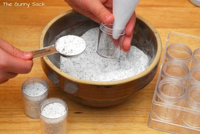 hands using a measuring spoon and a funnel to fill containers with the foot soak powder.