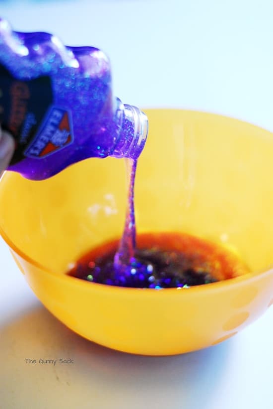 Pouring purple glitter glue from the bottle into a bowl.