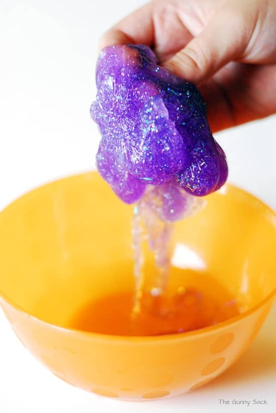 A hand removes the glittery slime from the bowl.