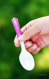 A hand holding a plastic spoon with a glittery handle.