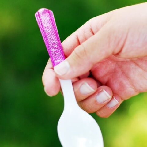 A hand holding a plastic spoon with a glittery handle.