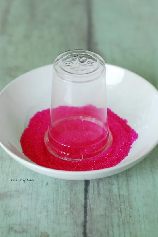 A plastic cup is dipped into pink sugar crystals.